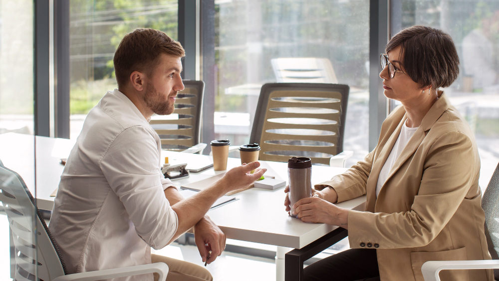 Two professionals having a focused one-on-one conversation in a modern office setting, demonstrating trust and open dialogue as part of fostering psychological safety.