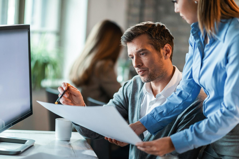 Two business professionals reviewing compliance in the workplace policies together at a modern office desk