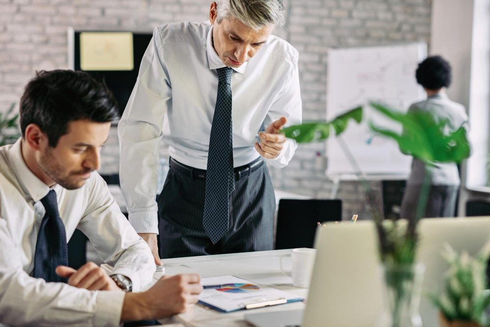 A manager gestures at a document to guide a seated employee, showing how performance standards are communicated.