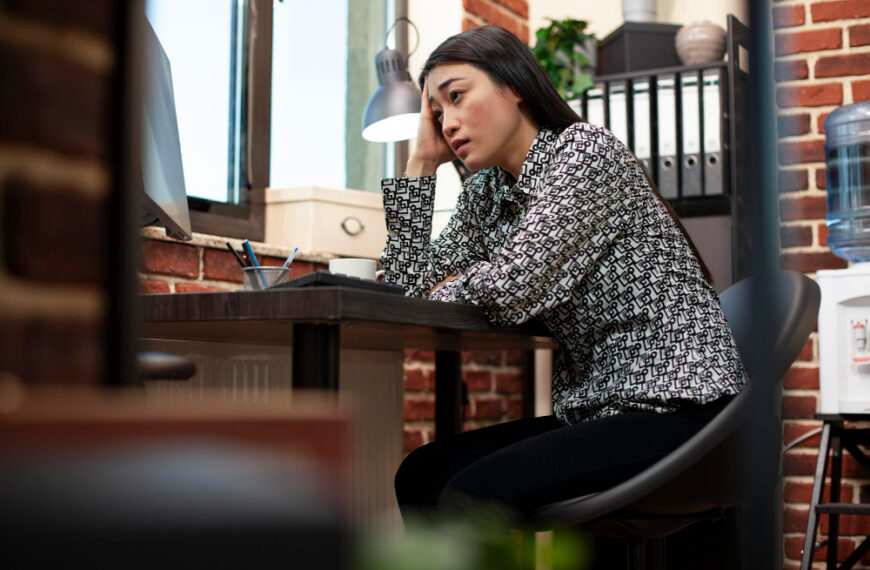 A stressed female employee rests her head on her hand at her desk, illustrating the strain of inconsistent performance.