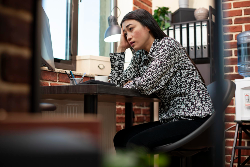 A stressed female employee rests her head on her hand at her desk, illustrating the strain of inconsistent performance.