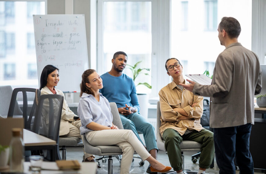 A male instructor presenting to a diverse group of seated employees during a workplace training session