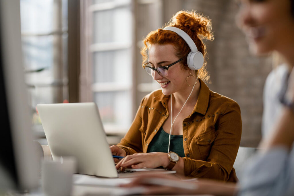 Smiling woman with headphones working at a laptop, reflecting training in the actual work environment.