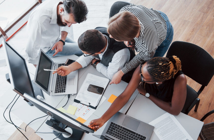 Overhead view of a team collaborating around a desk with laptops, illustrating real working conditions.