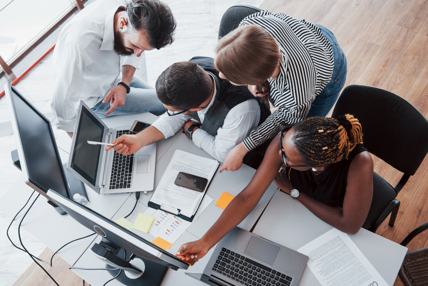 Overhead view of a team collaborating around a desk with laptops, illustrating real working conditions.